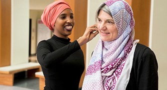 Image of a student helping a faculty member properly wear a hajib