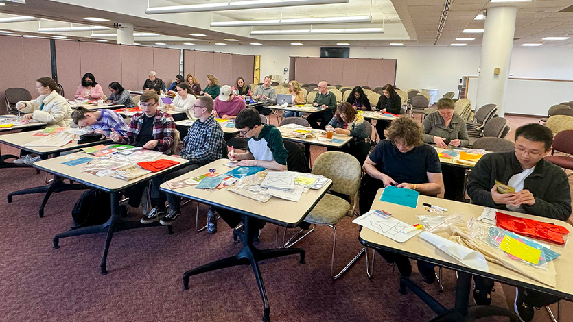 Image of students and alumni sitting at tables making comfort kits.